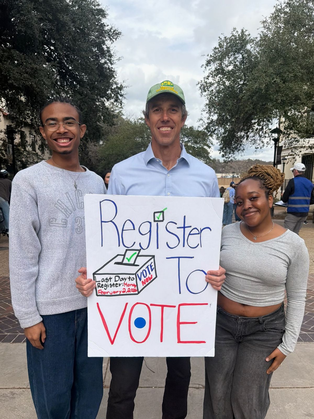 Beto holding a sign that says 'Register to Vote' with two students at Texas State.