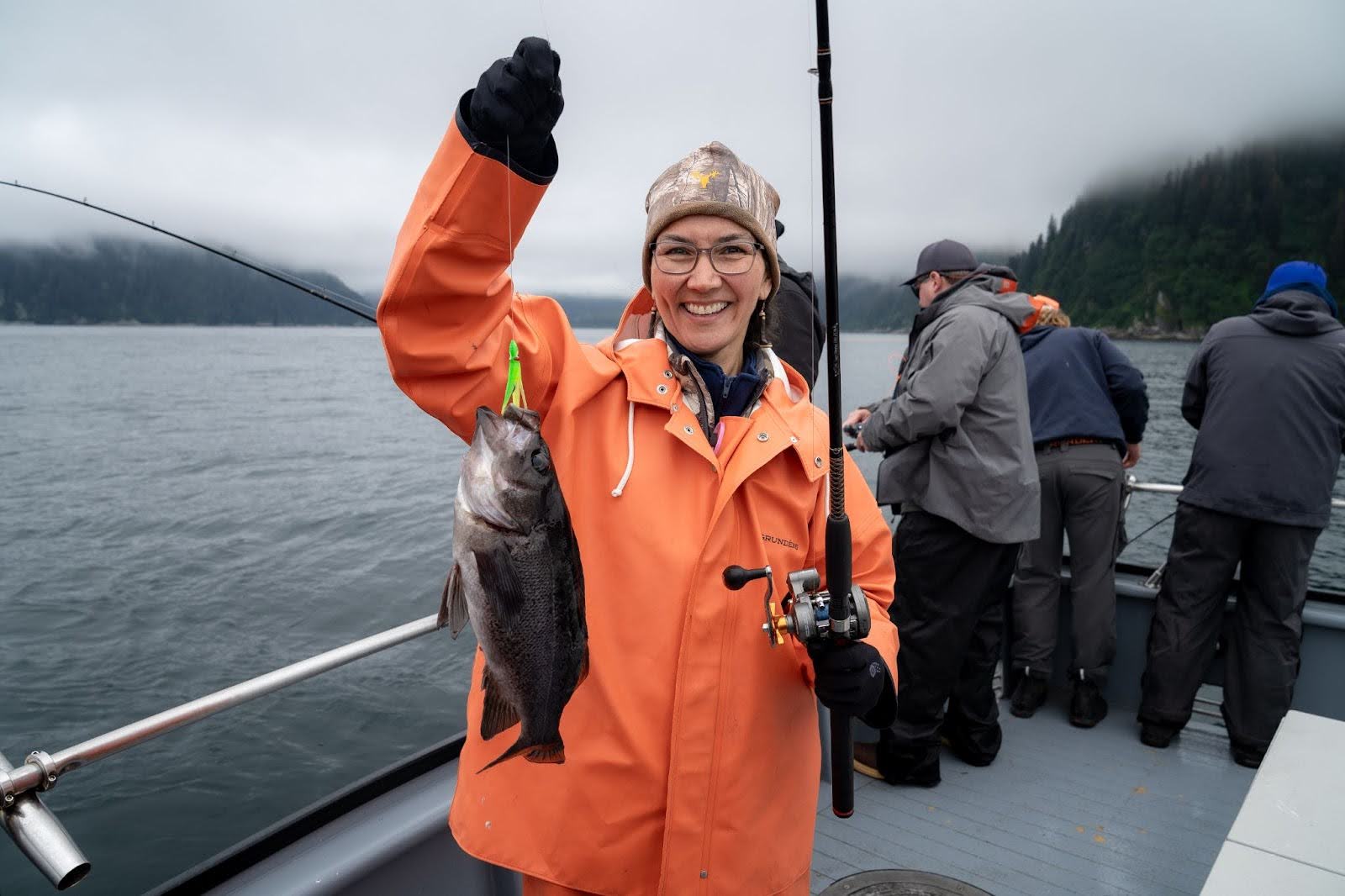Mary Peltola in an orange jacket on a boat holding a fish she caught