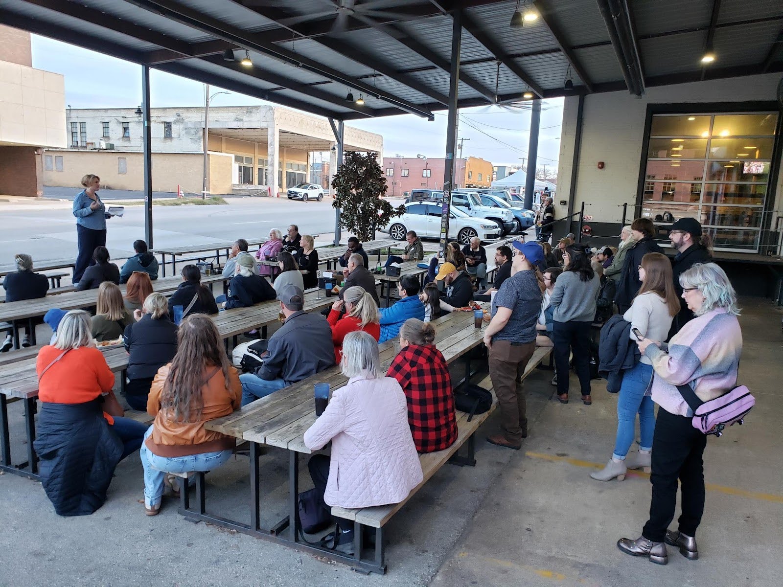 A person standing on a bench speaking in front of a seated crowd.